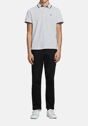 Hvid polo shirt med sorte kraveakcenter, parret med sorte bukser og hvide sneakers. Skjorten har et logo på brystet.