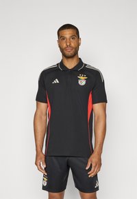 Czarna koszulka polo z czerwonymi akcentami po bokach, z haftowanym logo i trzema gwiazdami. W komplecie czarne szorty, obie części z brandingiem Adidas.