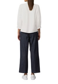 Chemisier blanc texturé à manches 3/4 associé à un pantalon en denim large bleu marine et des baskets blanches avec un détail d'accent à l'arrière.