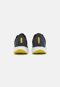 Zapatillas deportivas negras y grises con parte superior de malla, media suela blanca y acentos amarillos en la suela exterior. Presenta un patrón texturizado en el talón.