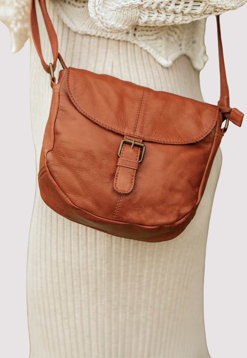 Ruda odinė per petį nešama tašė su sklendžio uždarymu, reguliuojamu dirželiu ir priekiniais sagties akcentais. Minkšta tekstūra ir apvalios formos.