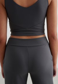 Szary sportowy top z dekoltem w kształcie litery V z tyłu oraz pasujące legginsy z wysokim stanem, charakteryzujące się gładką fakturą i minimalistycznym brandingiem.
