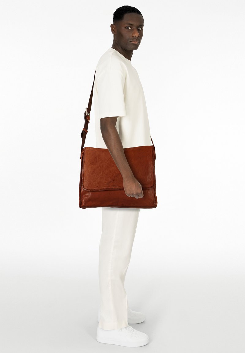 Borsa messenger in pelle marrone con una texture liscia, dotata di chiusura a patta e tracolla regolabile, tenuta in posizione eretta.