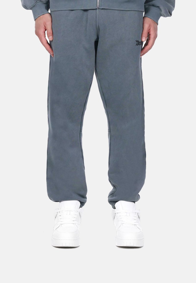 Pantalons de survêtement gris avec une coupe décontractée, dotés d'une taille élastique et de poches latérales. Associés à des chaussures de sport blanches, offrant un look décontracté.