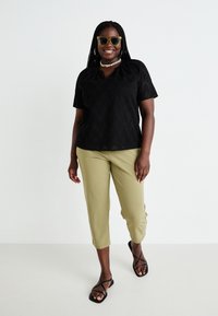 Svart kortärmad topp med texturmönster, kombinerad med olivgröna cropped-byxor och svarta sandaletter med remmar, accessoriserad med solglasögon.