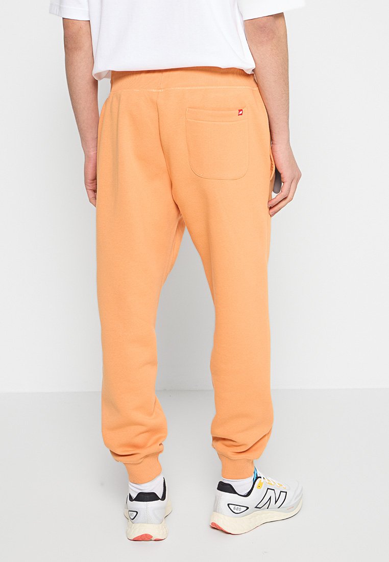 Pantalones de chándal anchos de color naranja, hechos de una tela suave, con una cinturilla acanalada y un bolsillo trasero. Combinados con zapatillas blancas y negras.
