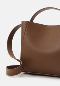 Brun läderhandväska med en strukturerad design och bred, platt handtag. Har en sömlös utsida och en slät yta.