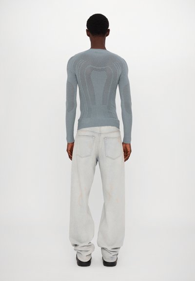 Lichtblauwe gebreide trui met een gestructureerde, gemusterde achterkant, gecombineerd met losse, lichte spijkerbroek. De outfit heeft een modern, casual ontwerp.