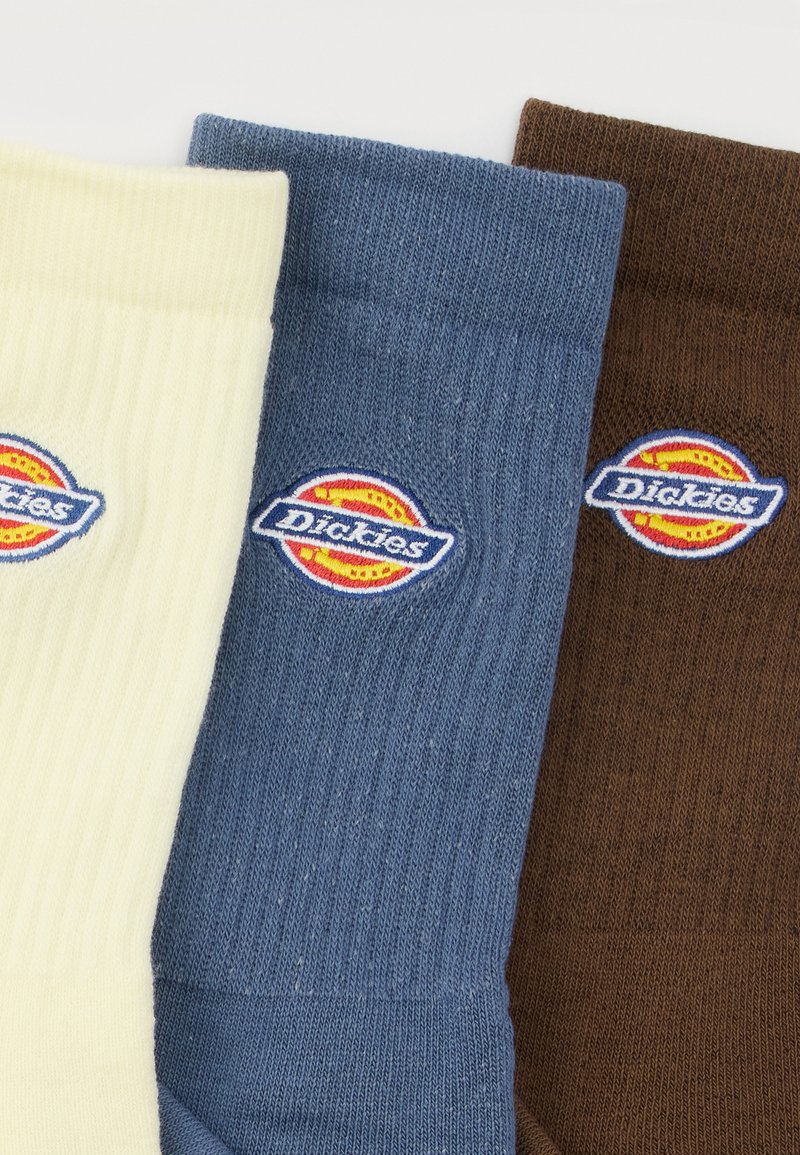 Drei gerippte Kurzsocken in Creme, Blau und Braun, jeweils mit einem farbigen, aufgenähten Dickies-Logo-Patch nahe dem oberen Rand.