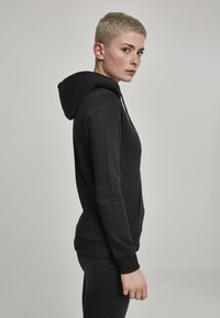 Black hoodie with a fitted design, soft fabric, ribbed cuffs, and a kangaroo pocket. Features a drawstring hood and smooth texture.