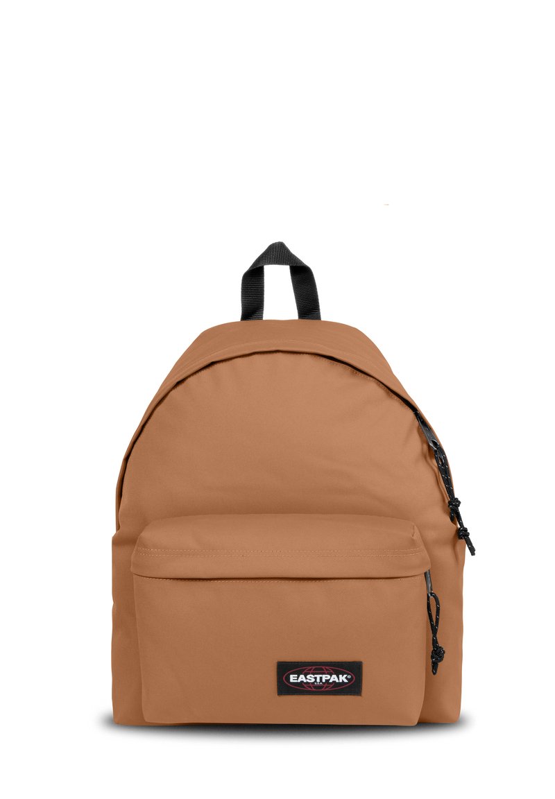 Mochila de tela color beige con forma redondeada, bolsillo frontal con cremallera y parche de logo negro. Cuenta con correas de hombro acolchadas y un asa en la parte superior.