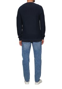 Navy gebreide trui met geribde manchetten en onderkant, gecombineerd met lichtblauwe denim jeans en witte sneakers, gezien van achteren.