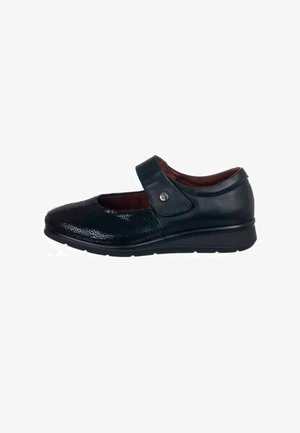 Zapato Mary Jane de cuero negro con superficies texturizadas, correa ajustable y suela baja en cuña. Presenta un acento metálico circular en la correa.