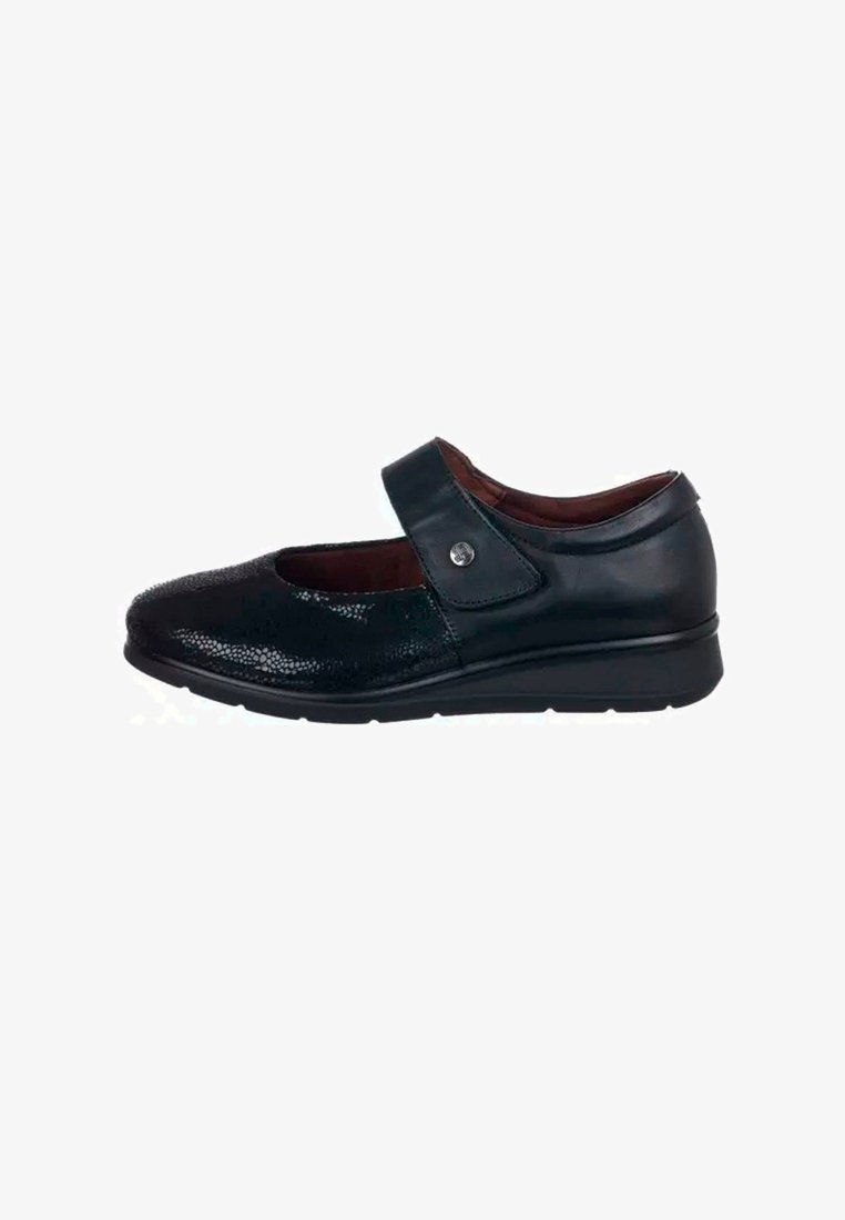 Zapato Mary Jane de cuero negro con superficies texturizadas, correa ajustable y suela baja en cuña. Presenta un acento metálico circular en la correa.
