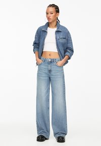 Lichtblauwe denim jacket met een cropped snit, gecombineerd met wijdvallende lichtblauwe jeans. Zwarte platformschoenen, met een zachte textuur en subtiele stiksels.