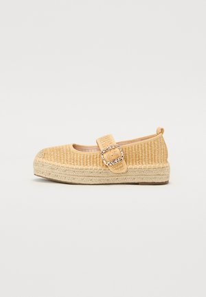 Beige vævet flad sko med en tyk jute sål og en bred rem fastgjort med en stor dekorativ metalspænde.