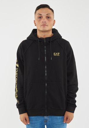 Felpa nera con zip realizzata in tessuto morbido, dotata di tasca a marsupio e logo EA7 giallo sul petto e sulla manica. Presenta un cappuccio con coulisse.