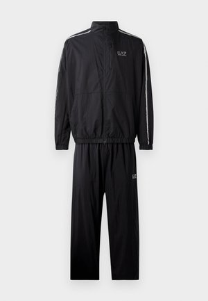 Black tracksuit with a zip jacket and elastic waist pants, featuring white side stripes and logo on the chest and thigh. Textured material.
