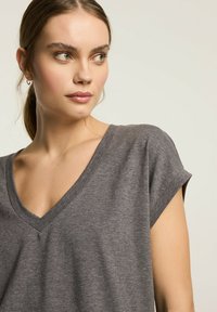 Szary, krótki rękaw T-shirt z dekoltem w kształcie litery V, wykonany z miękkiego materiału, charakteryzujący się luźnym krojem i subtelną teksturą, z minimalnymi detalami szycia.