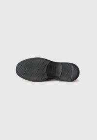 Semelle de chaussure noire avec un motif de grip texturé, comportant des lignes horizontales et diagonales, des bords lisses et une empreinte de logo.