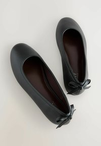 Melni ādas baleta dzīvokļi ar apaļu purngalu, plakanas zolītes un mazu lentītes loku uz papēža. Gluda tekstūra un vienkāršs dizains.