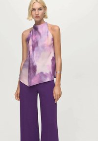 Haut sans manches à motifs violets et roses avec un design drapé, associé à un pantalon large violet. Texture de tissu lisse.
