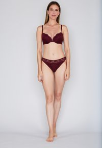 Burgundy lace bra with underwire and adjustable straps, paired with matching lace thong. Smooth texture, delicate floral pattern.