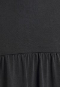 Robe noire en tissu côtelé, dotée d'un corsage ajusté et d'une jupe évasée avec volants. Texture douce, apparence lisse, aucun motif visible.