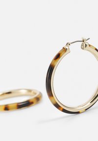 Schildpadmotief oorbellen in de vorm van een ring met een gouden sluiting. Flexibel plastic materiaal met bruine en beige patronen. Lichtgewicht ontwerp.