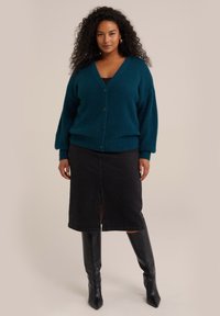 Teal, fluffig cardigan med V-hals och knappstängning, ihop med en svart denimkjol med en framslits och knähöga svarta stövlar.