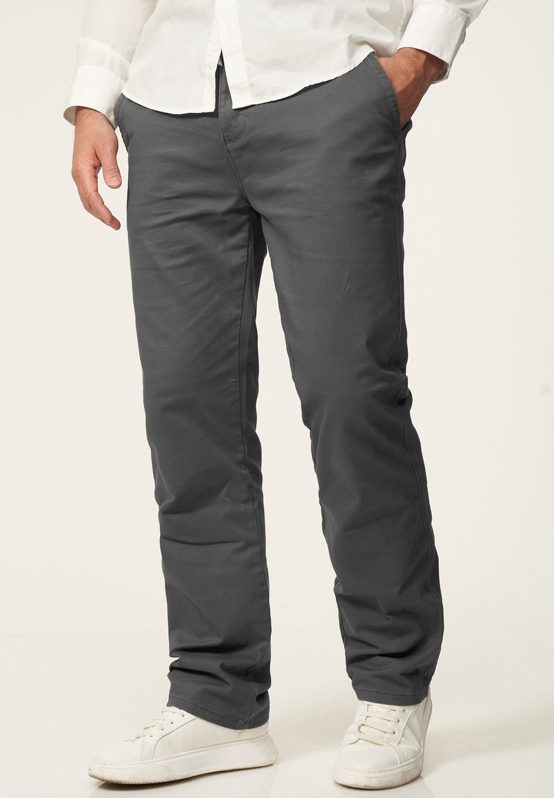 Grey, straight-leg pants made of cotton blend fabric, featuring side pockets and a smooth finish, paired with white sneakers.