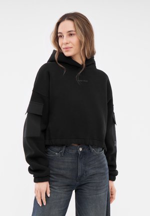 Black cropped hoodie with a drawstring and front pocket. Ribbed cuffs and hem, featuring side patch pockets and printed logo detail.