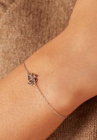 Sterling silver bracelet with a fluid, curved design. Adjustable chain attachment, worn on a wrist over a light brown textured fabric.