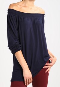 Granatowa bluzka bez ramiączek wykonana z miękkiego materiału, z marszczonym dekoltem i długimi rękawami, w połączeniu z bordowymi spodniami.