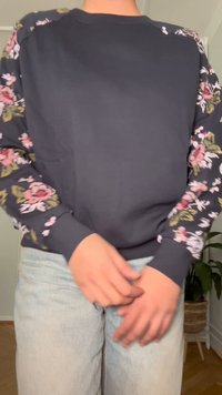 Tmavosivý sveter s kvetinovým vzorom na rukávoch v ružovej a zelenej farbe. Manžety a spodný lem sú v jednofarebnej tmavosivej farbe. Mäkko tkanina, voľný strih.
