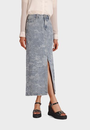 Gonna midi in denim di colore azzurro chiaro, con intricati motivi bianchi e uno spacco frontale. Abbinata a sandali con tacco a cuneo neri.
