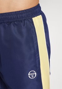 Námořnické sportovní šortky se žlutým pruhem, elastickým pasem a logem; vyrobené z lehké, texturované tkaniny; obsahují detaily po stranách.