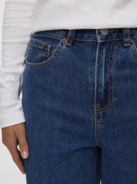 Temno modre kavbojke z ravnim krojem hlačnic, z vidnim šivom, sprednjim gumbom in stranskimi žepi. Oblečene z belo dolgimi rokavi.