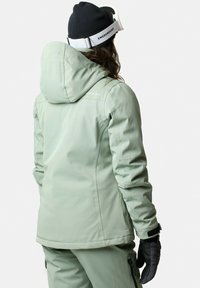Light green ski jacket with a hood, featuring a smooth, waterproof texture, elastic cuffs, and two side pockets. Black gloves worn on hands.