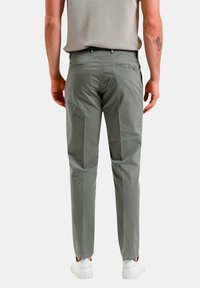 Pantaloni grigi chiari con una vestibilità slim, dotati di tasche posteriori e una texture liscia. Abbinati a sneaker bianche.