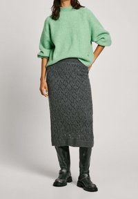 Lichtgroene geribbelde sweater met verlaagde schouders, gecombineerd met een donkergrode gebreide rok met een ruitpatroon en zwarte kniehoog boots.