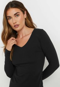 Maglietta nera a maniche lunghe con scollatura a V, realizzata in tessuto morbido. Presenta un design aderente e una tasca piccola sul lato sinistro.