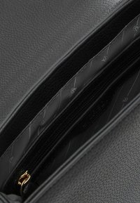Interno della borsa in pelle nera caratterizzato da una superficie testurizzata, un compartimento con zip e un rivestimento in tessuto con un sottile motivo geometrico.