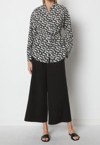 Camicia a righe bianche e nere con vita aderente, bottone sul davanti, polsini a contrasto e pantaloni neri larghi. Abbinata a sandali neri a infradito.