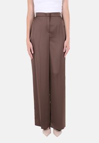 Pantaloni marroni a vita alta con gamba larga, pieghe anteriori e consistenza liscia. Abbinati a scarpe color chiaro con punta affusolata.