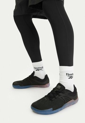 Legs wearing black athletic leggings, white Reebok crew socks, and black Reebok low-top sneakers with translucent blue soles.