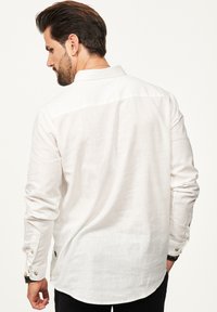 Weißes Langarmhemd aus strukturiertem Stoff, mit abgerundetem Saum, Knopfmanschetten und klassischem Kragen. Rückansicht gezeigt.