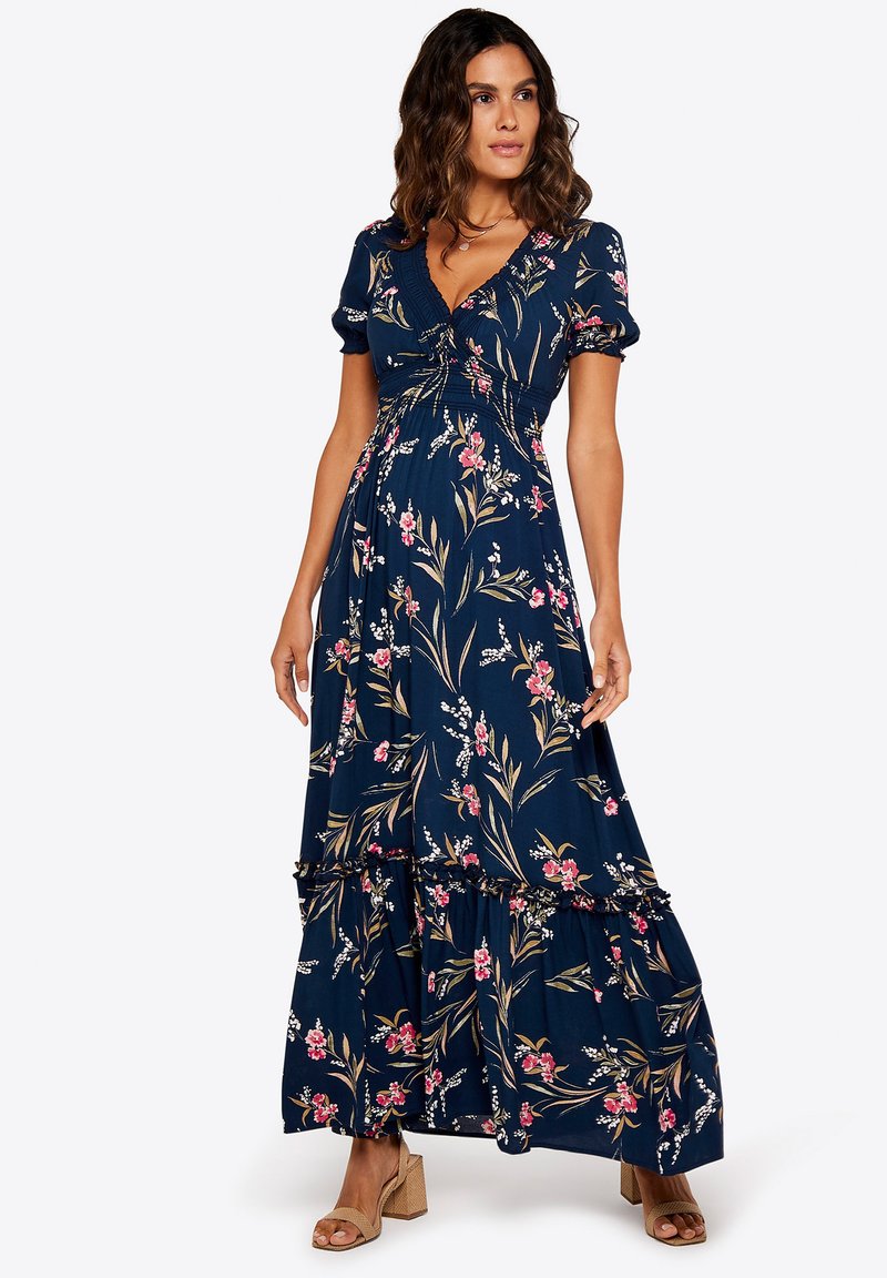 Blommig maxiklänning i marinblått med korta puffärmar, V-ringning, lager på lager volangkant, och rosa och vita blommönster genom hela klänningen.