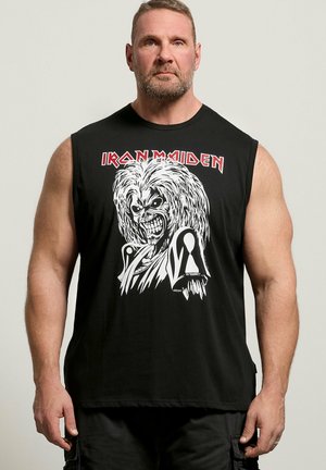 Uomo muscoloso con capelli corti che indossa una maglietta nera senza maniche degli Iron Maiden con una grafica bianca di un volto ringhiante con capelli selvaggi.