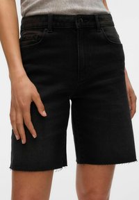 Shorts de mezclilla negra con dobladillo deshilachado, diseño de cinco bolsillos y cierre de botón. La tela parece resistente con una textura sutil.